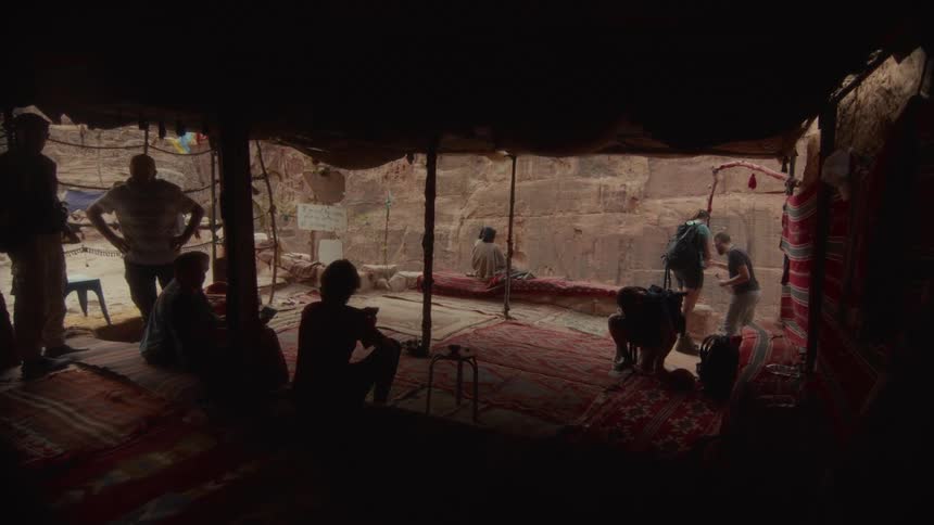 A group of hikers relax and take a break inside a traditional tent with a view of a desert canyon