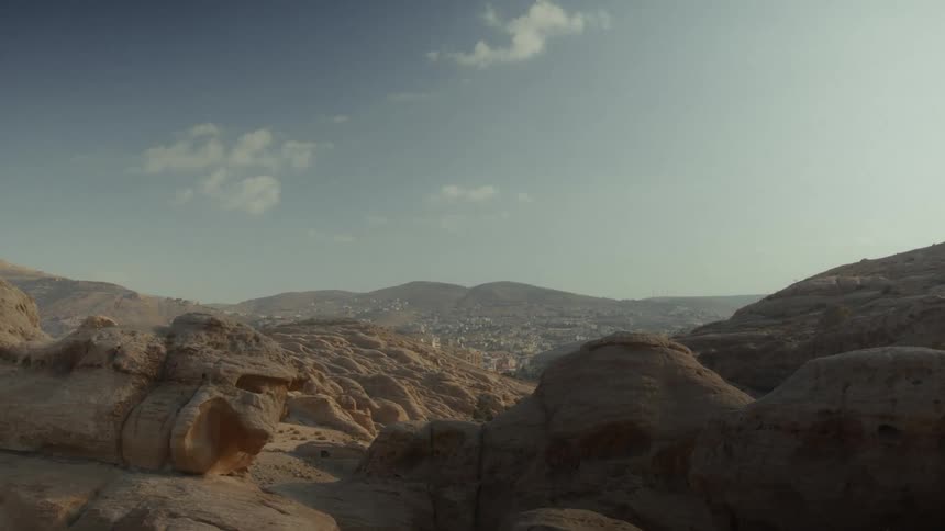 A slow zoom reveals a modern city nestled in a valley surrounded by the vast, rocky desert landscape of Petra, Jordan