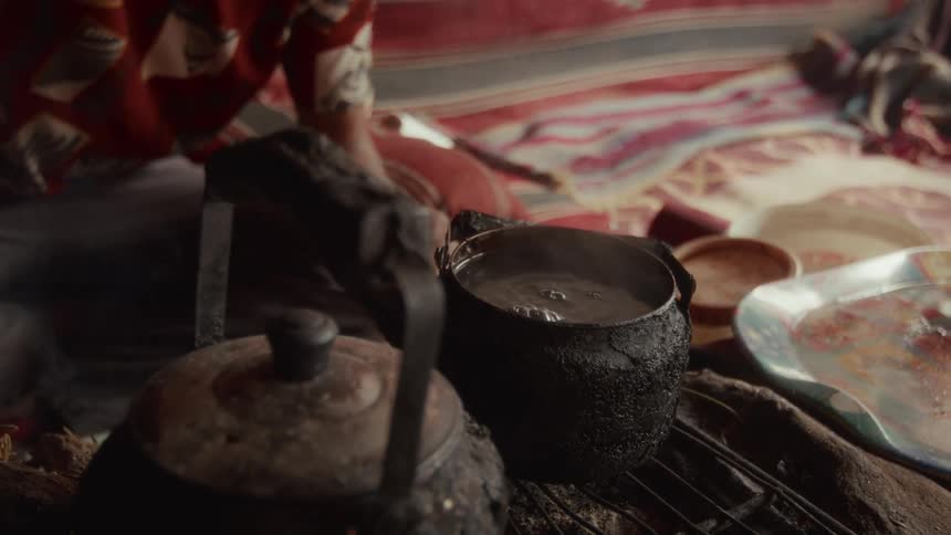 Close-up of a traditional tea-making ritual as a person pours hot, steaming water into a blackened kettle over a fire