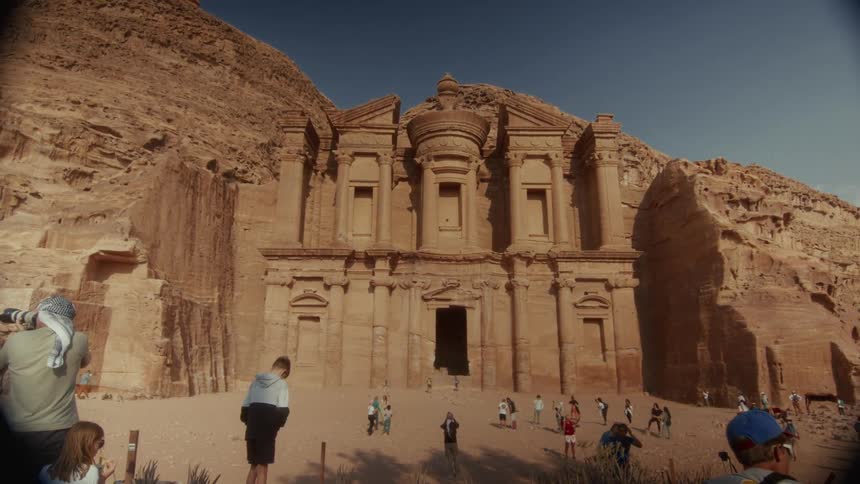 Tourists gather to admire the magnificent Ad-Deir Monastery carved into the sandstone cliffs of Petra on a sunny day