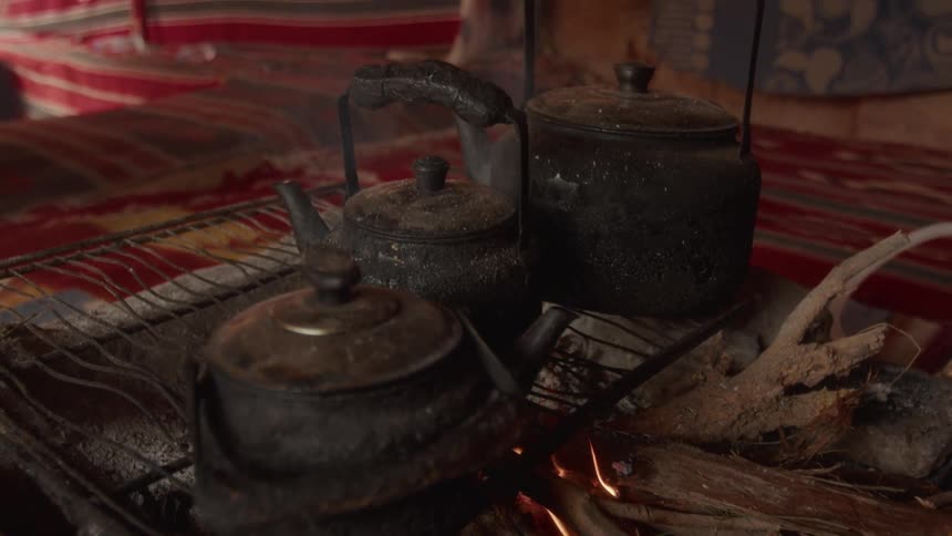 Three old soot-covered teapots heat up over a smoldering campfire in a traditional Bedouin tent