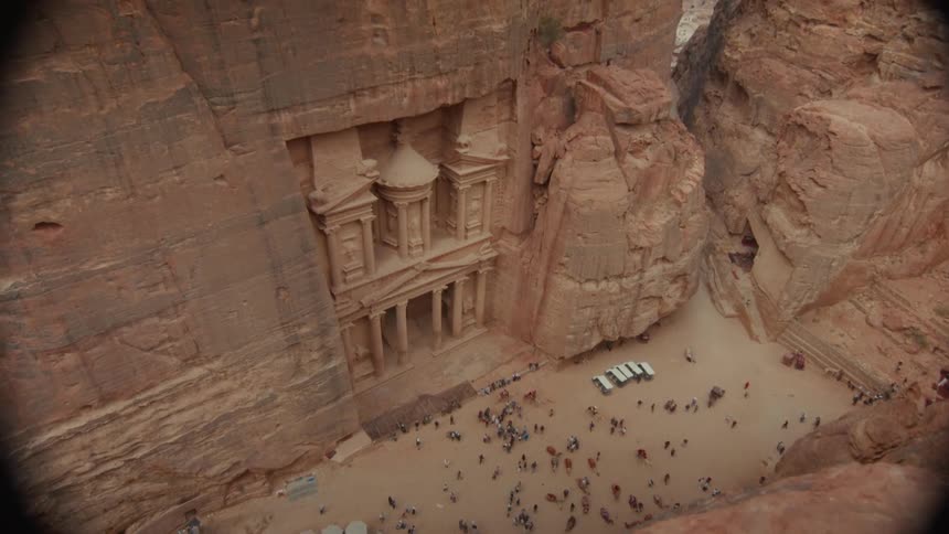 A first-person perspective from a cliff's edge reveals the stunning ancient Treasury of Petra in Jordan below