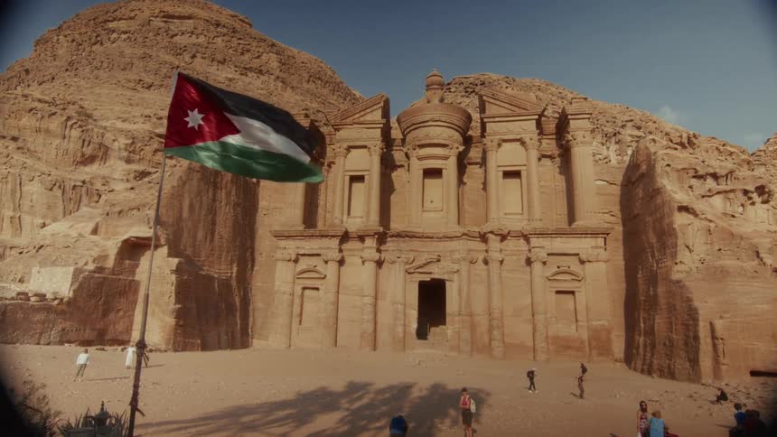 A static wide shot of the magnificent Ad-Deir Monastery in Petra, with the Jordanian flag waving in the foreground