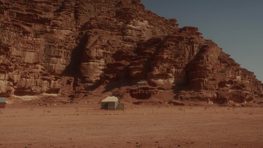 A solitary tent stands dwarfed by the immense red rock formations of the Wadi Rum desert in Jordan