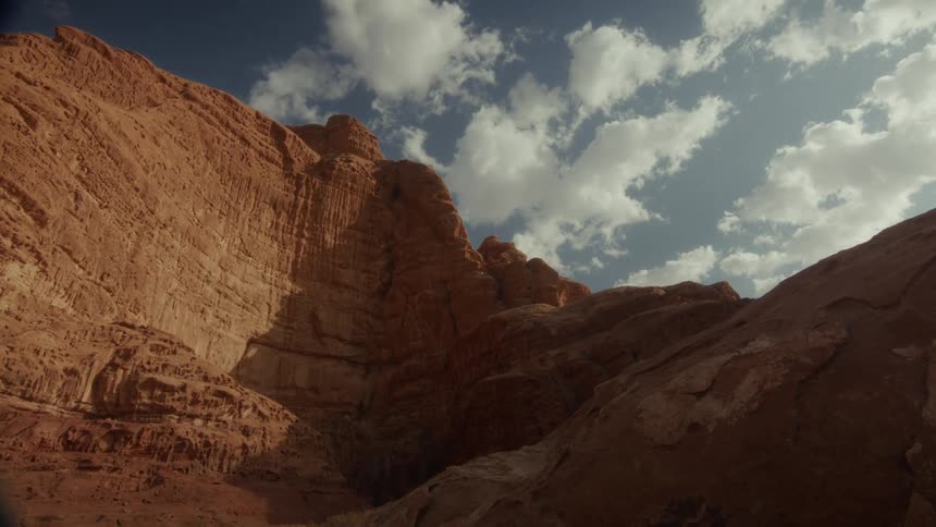 A low angle shot captures the immense scale of red rock canyon walls against a partly cloudy blue sky