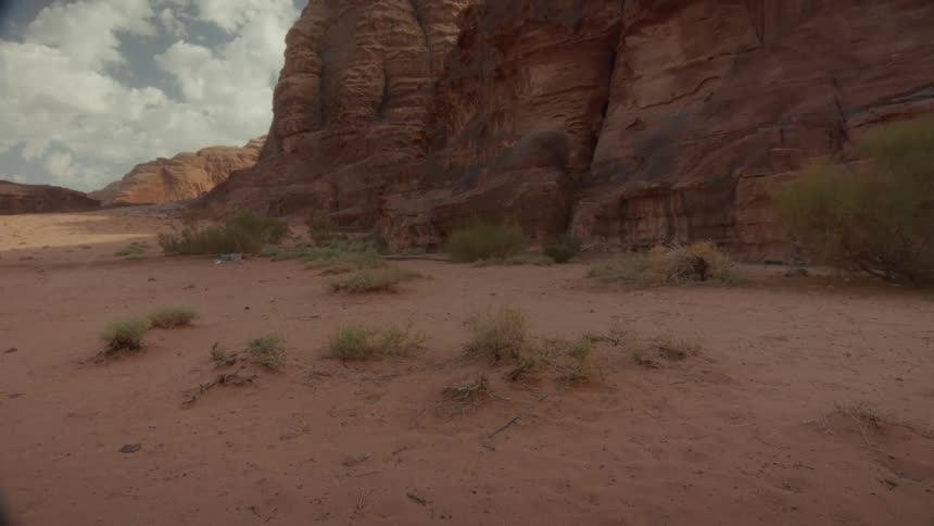 Wide shot of a majestic red rock formation in a sandy desert under a partly cloudy sky