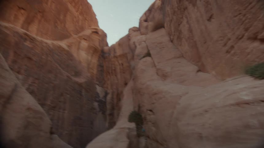 A slow camera pull-back reveals the vast, towering walls of a narrow red sandstone canyon