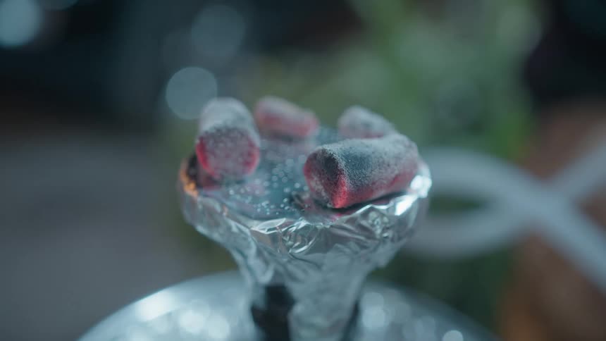Close-up of smoldering hot coals on a hookah bowl with smoke drifting in the background