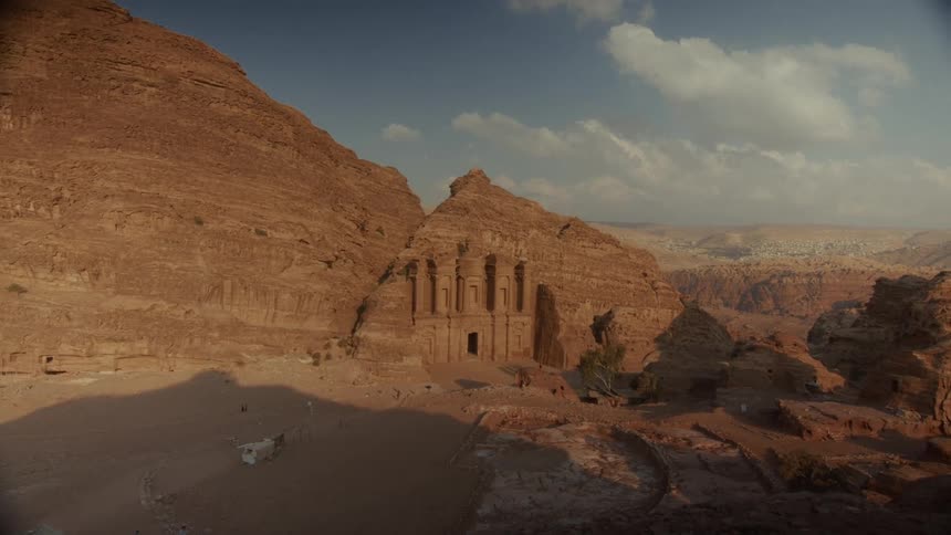 Golden hour sunlight casts long shadows across the magnificent Monastery (Ad-Deir) carved into the sandstone mountains of Petra, Jordan