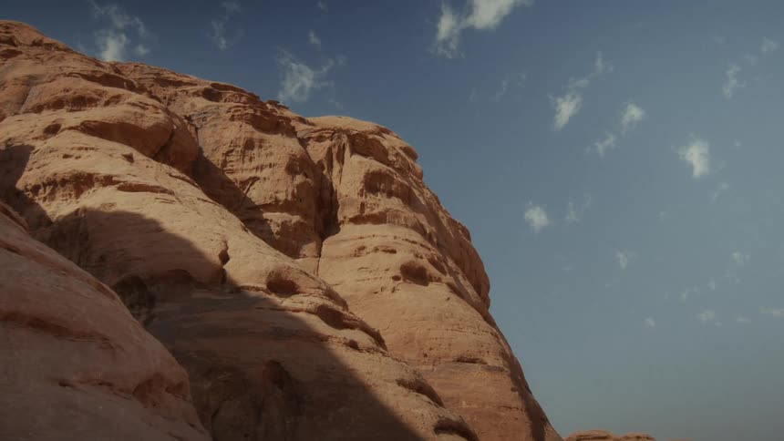 A sunlit, weathered rock formation towers against a clear blue sky with a few wispy clouds