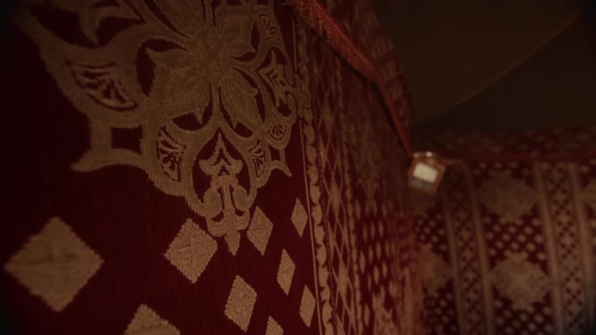 A close-up shot pans across the ornate red and white patterned fabric walls inside a dimly lit traditional tent