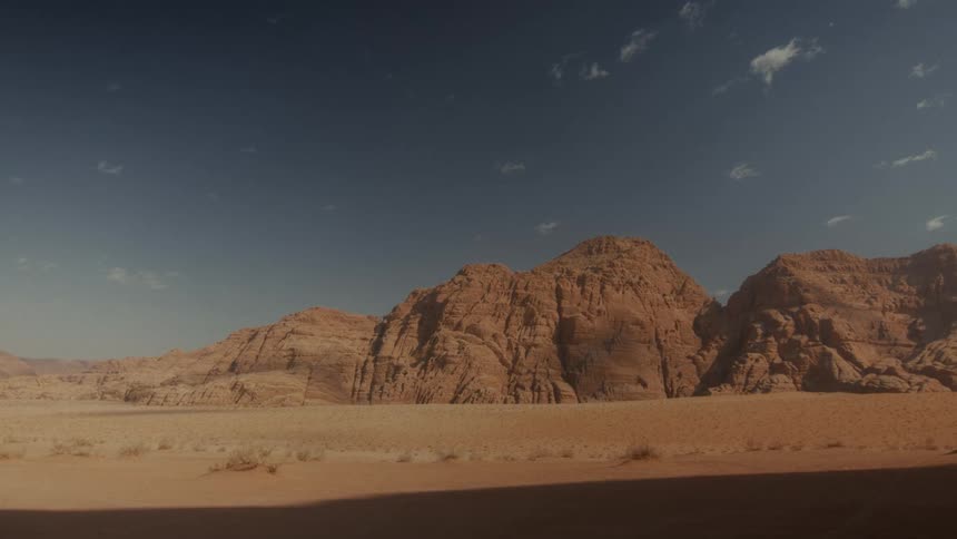 A wide, static shot of the vast, arid landscape of the Wadi Rum desert in Jordan under a clear blue sky