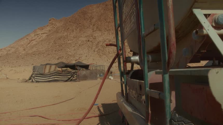 A water truck with a hose provides essential water to a remote Bedouin camp in the dry desert