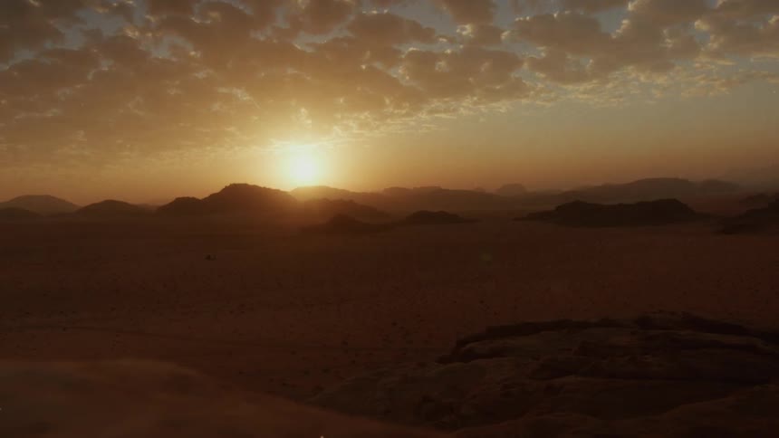 A stunning time-lapse captures the sun setting behind distant mountains, casting a golden glow over a vast desert landscape