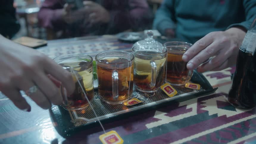 A tray of steaming hot tea in glass mugs is served to a group of friends who then pick up their cups in slow motion