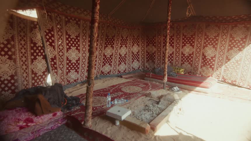 Slow tilt down revealing the interior of a traditional Bedouin desert tent with carpets and cushions on a sand floor