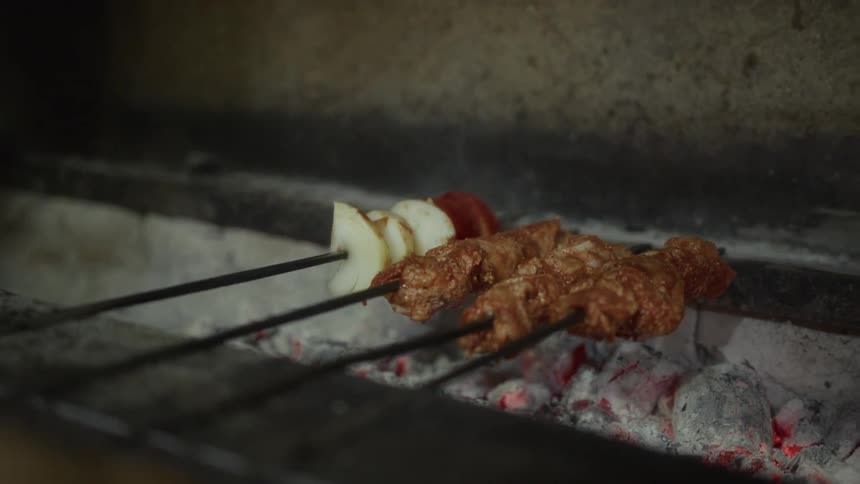 A close-up view of traditional Turkish adana kebab and vegetable skewers cooking over a hot charcoal grill