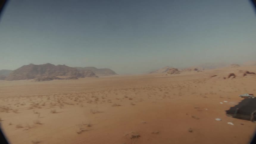 A wide, panning shot reveals a desolate camp with trucks in the middle of a hot, hazy desert