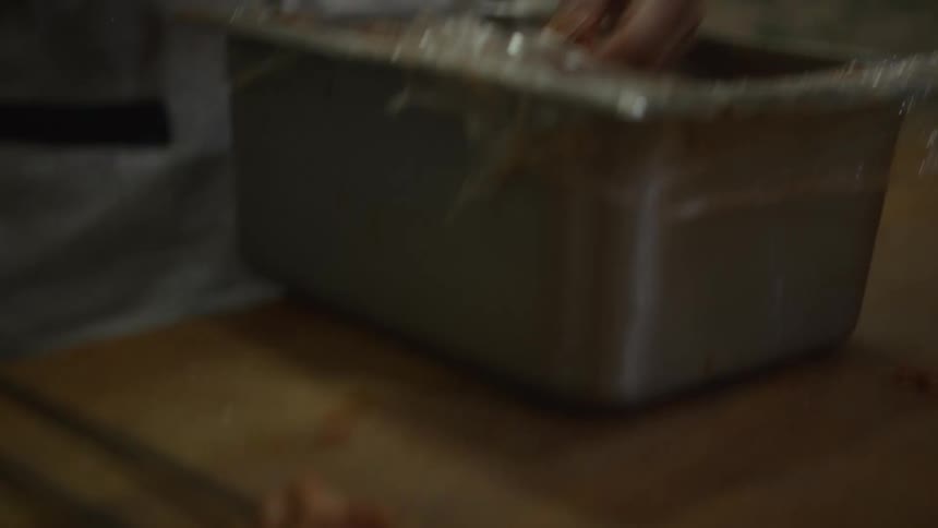 A chef carefully prepares raw seasoned meat on metal skewers in a dimly lit kitchen