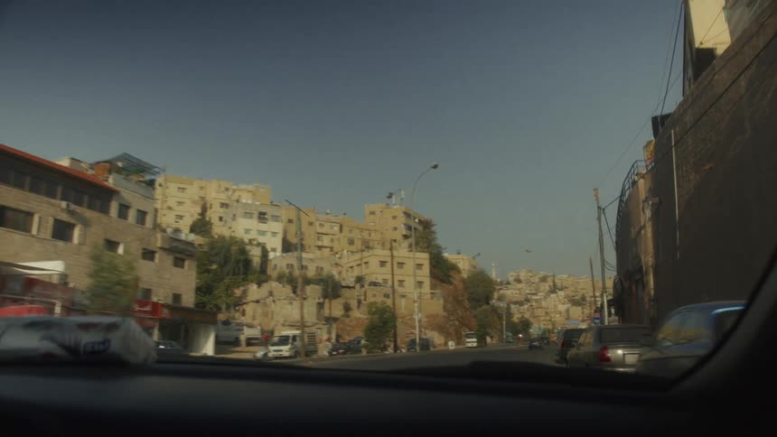Driving through the sunlit streets of a hillside city in the Middle East, captured from a car's perspective