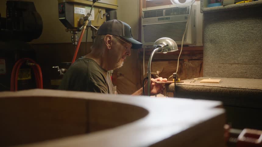 A focused luthier meticulously works on a small, intricate piece for a custom guitar in his workshop