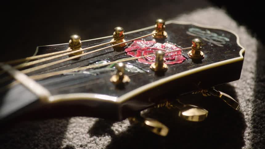 An artistic close-up reveals the detailed rose inlay on the headstock of a classic acoustic guitar under dramatic lighting