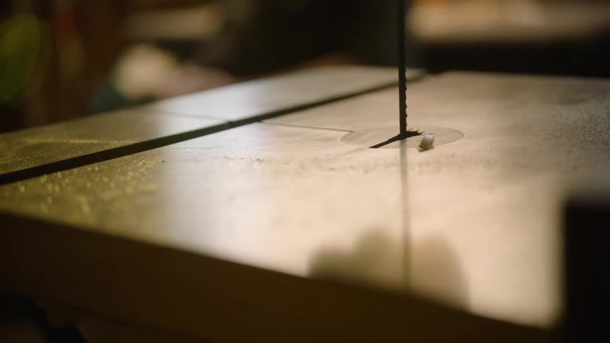 A close-up of a band saw blade running in a dimly lit workshop, with sawdust on the table