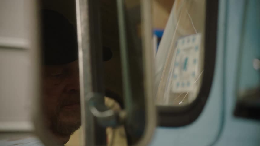 A moody close-up shot of a pensive older man's reflection in the side-view mirror of his vintage truck parked in a dimly lit garage