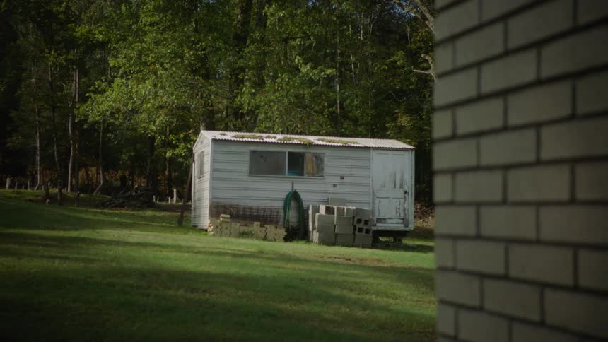 A slow focus reveals an old, rundown shed sitting in a grassy backyard with trees in the background