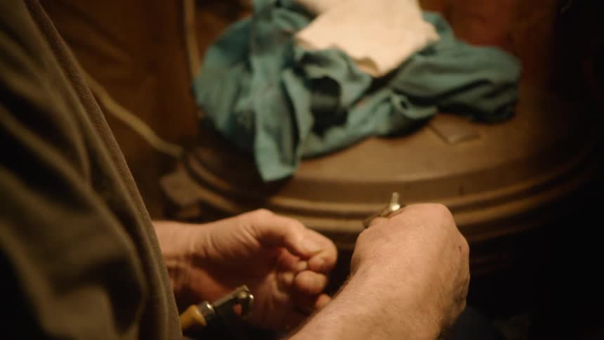 Close-up of a man's hands carefully wrapping thread to create a custom fishing fly lure in his workshop