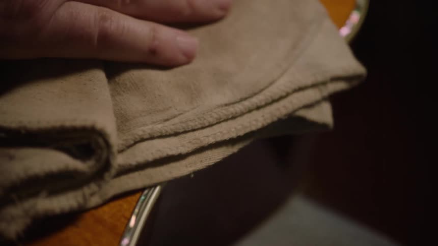 A person carefully polishes the beautiful wooden body and mother-of-pearl inlay of an acoustic guitar in slow motion