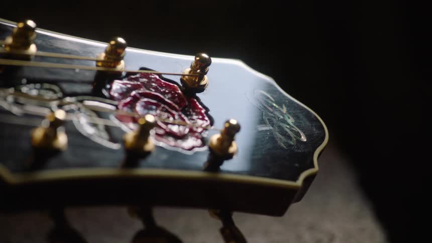 Intricate red rose and mother-of-pearl inlays adorn the headstock of a custom acoustic guitar in this dramatic close-up shot