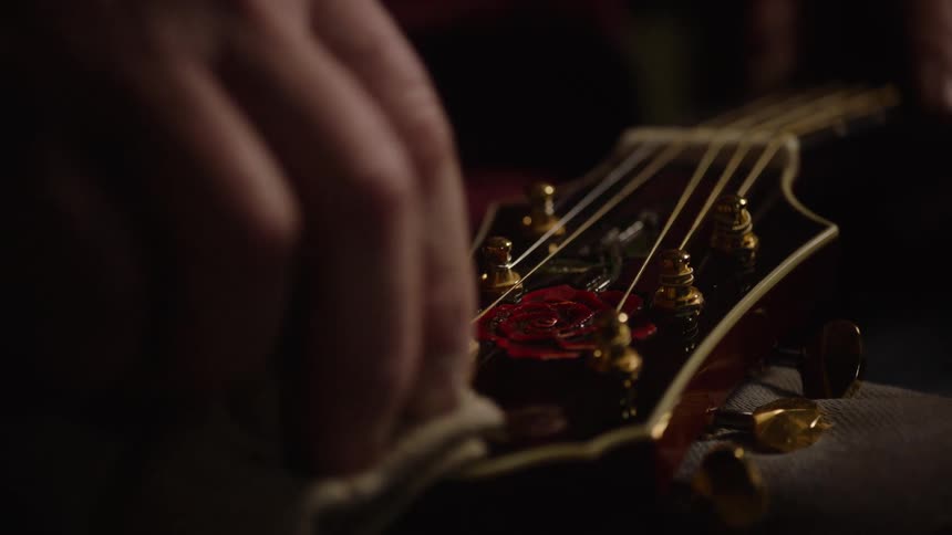 A musician carefully polishes the beautiful headstock of their acoustic guitar with a soft cloth