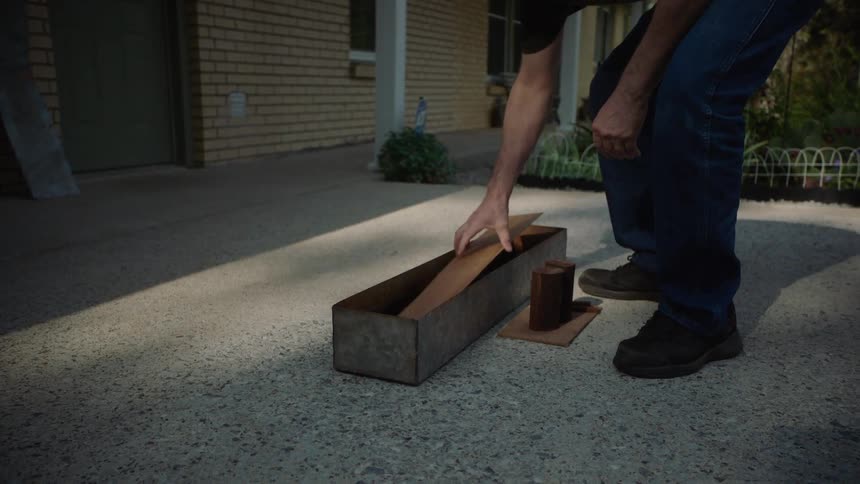 A craftsman carefully assembles a wooden mold inside a long metal box in slow motion