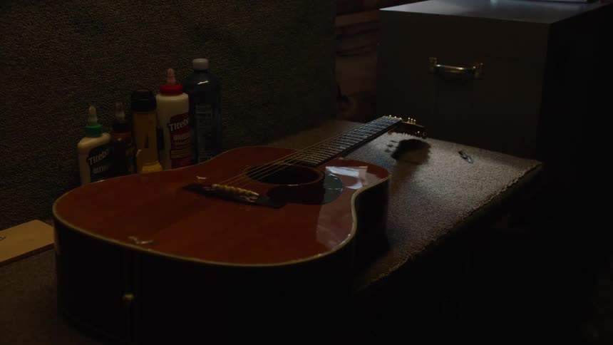 A slow zoom out reveals an acoustic guitar resting on a workbench in a dimly lit workshop