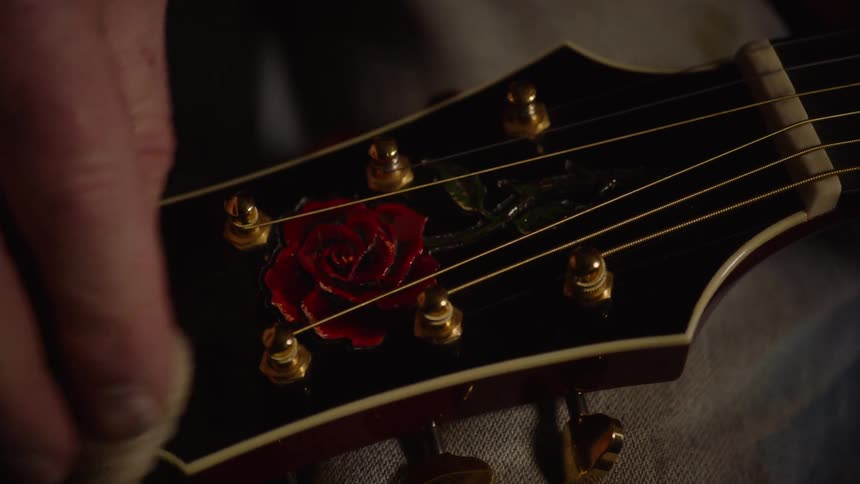 A close-up shot of a hand carefully polishing the headstock of an acoustic guitar adorned with a red rose inlay