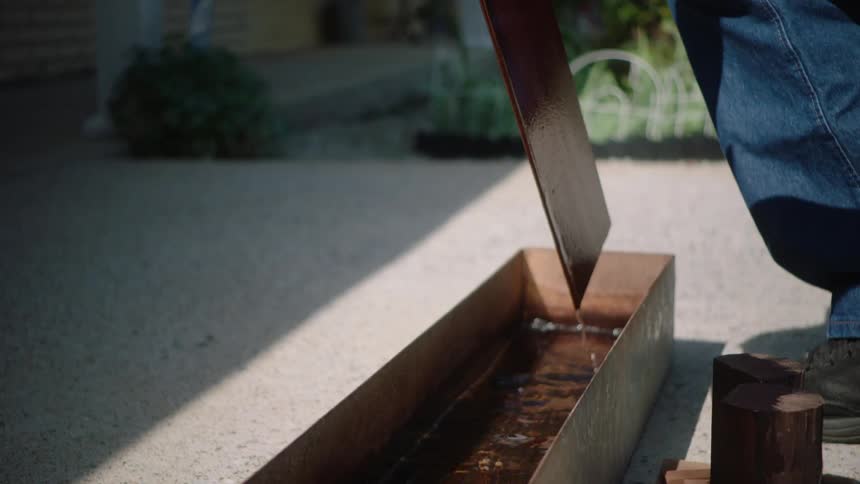A craftsman's hand carefully lifts a thin piece of wood from a water bath in stunning slow motion