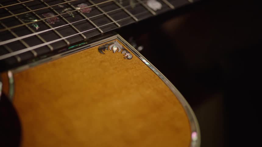 Artistic close-up shot slowly pans across the body and neck of an ornate acoustic guitar
