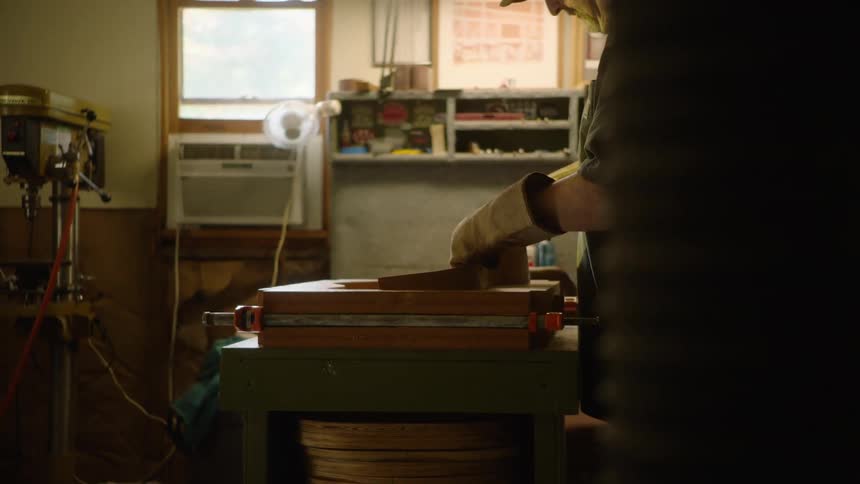 A luthier carefully removes a newly bent piece of wood from a mold in his workshop