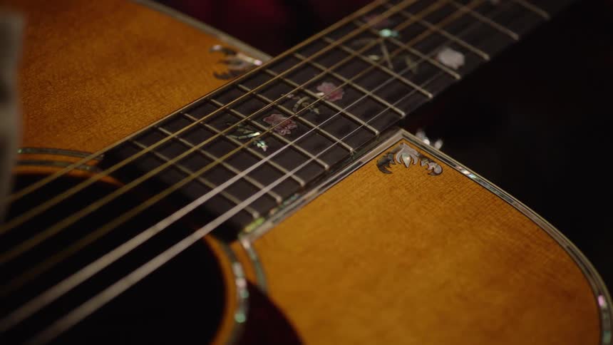 A musician meticulously cleans their ornate acoustic guitar with a soft cloth, polishing the wood and decorative fretboard inlays
