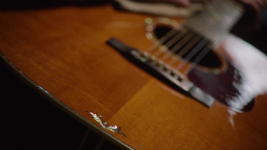 A craftsman with a warm expression carefully cleans and polishes his beloved acoustic guitar in his dimly lit workshop