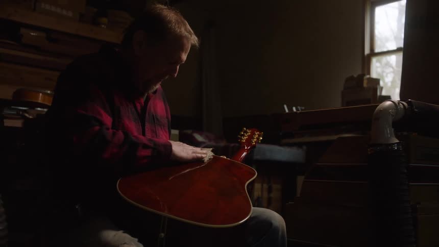 A dedicated luthier gently polishes a newly crafted acoustic guitar in his rustic, dimly lit workshop