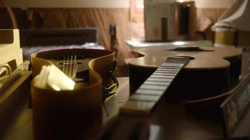 An intimate, slow pull focus reveals guitars and other string instruments on a luthier's workbench