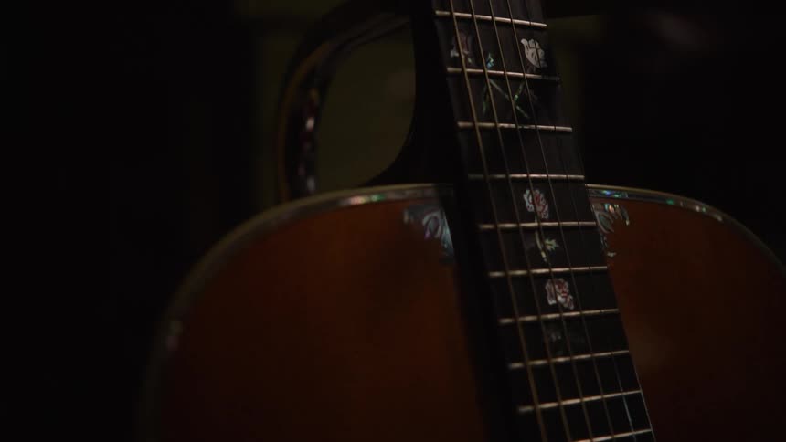 A slow and moody close-up shot reveals the intricate mother-of-pearl inlays on a wooden acoustic guitar