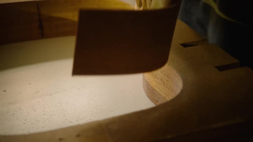 Skilled luthier carefully bends and shapes a piece of wood for a guitar body in a specialized mold