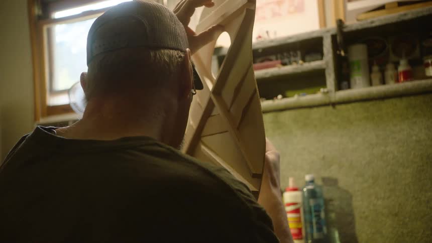 Over-the-shoulder shot of a skilled luthier carefully inspecting the intricate wooden bracing of a custom-built acoustic guitar in his workshop