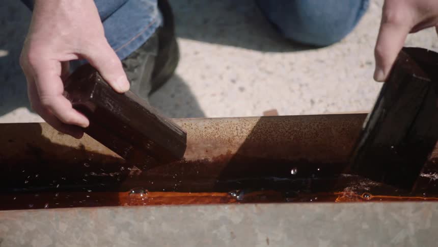 Close-up slow motion of a person's hands dipping dark wooden blocks into a trough of wood preservative