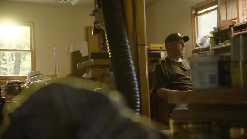 A craftsman sits in his sun-drenched workshop taking a thoughtful break from his work