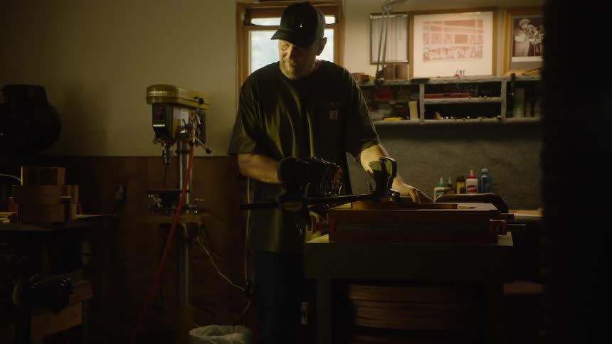 A senior craftsman meticulously works on a woodworking project using clamps and hand tools in his classic, warmly lit workshop