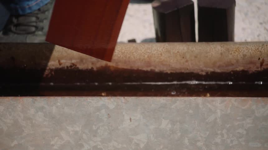 A close-up slow motion shot of wood stain dripping off a freshly treated plank into a metal trough